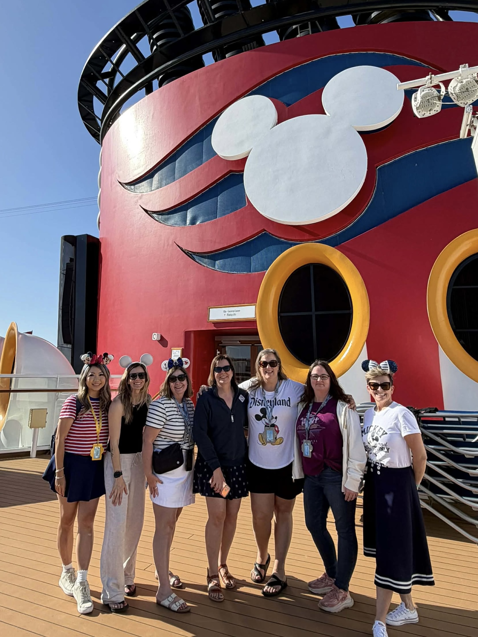:Pure Magic Vacations advisors standing on deck with the Disney Cruise Line funnel behind them.