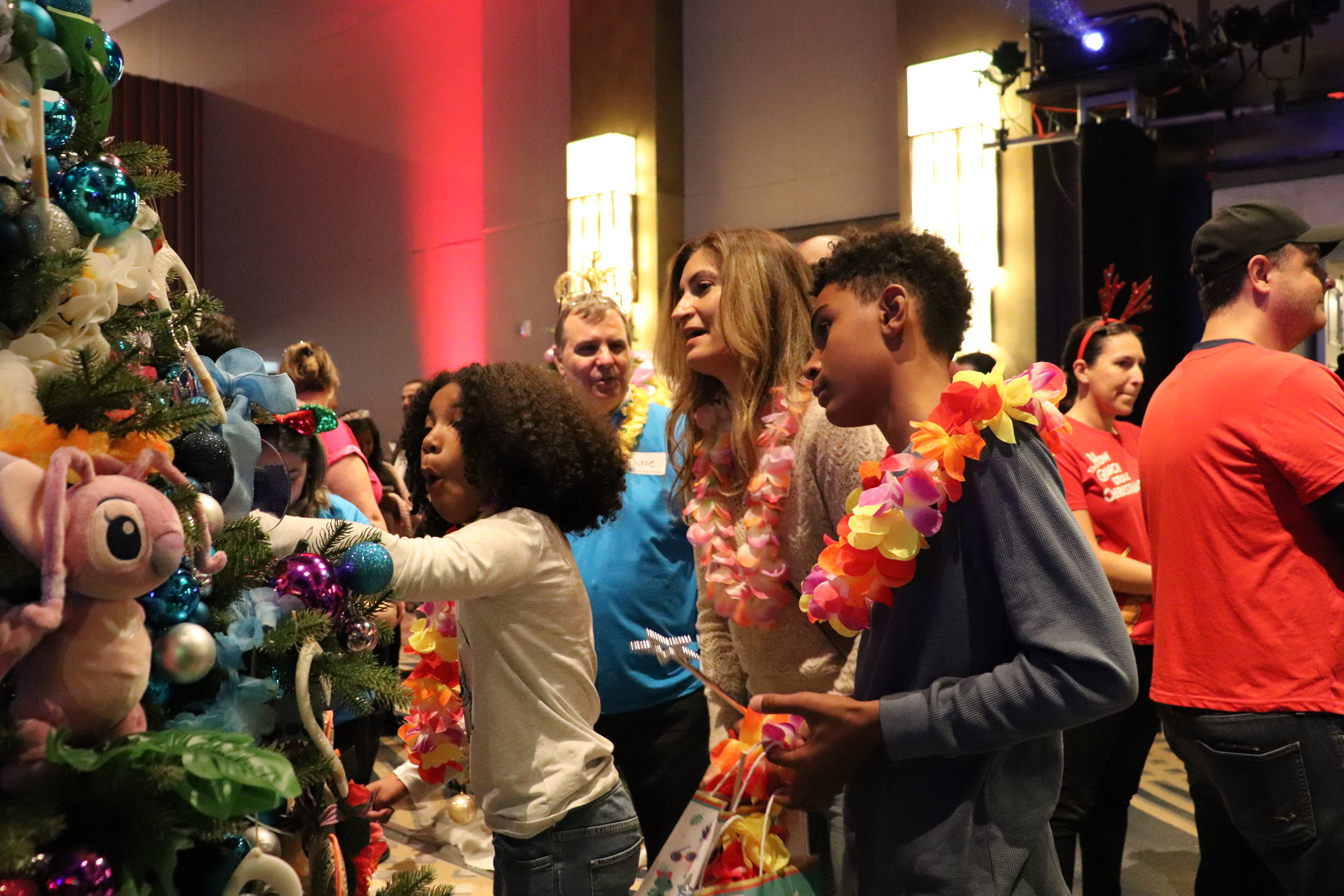  A child reaches towards decorations on a colourful Trees of Joy Christmas tree while other attendees look on.